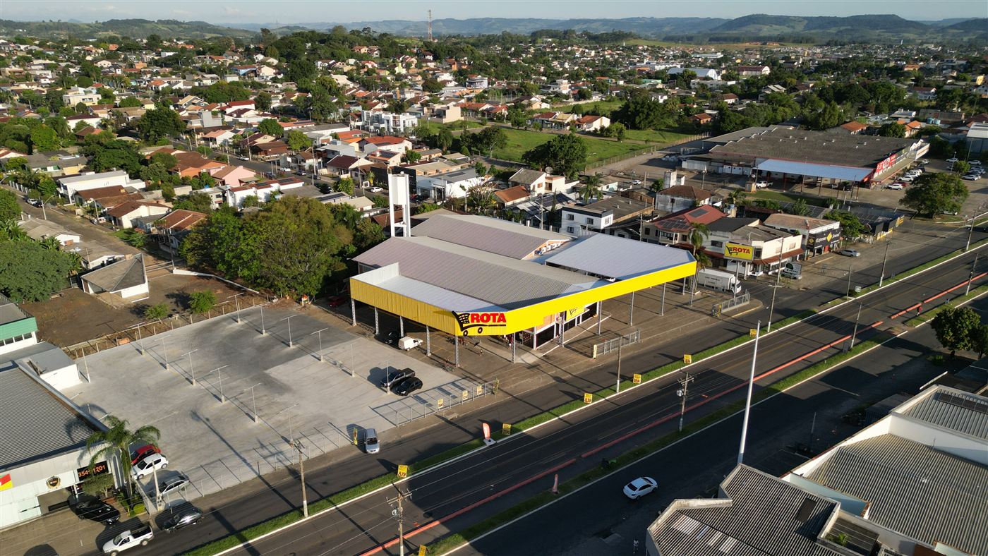 Vista aérea de pavilhão comercial com grande estacionamento na avenida